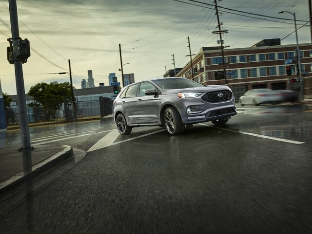 A 2024 Ford Edge® ST SUV in Iconic Silver being driven on a wet city road