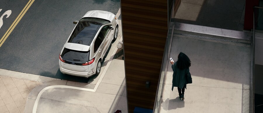 Woman holds a smartphone on a walkway overlooking her 2024 Ford Edge® SUV parked on the street below