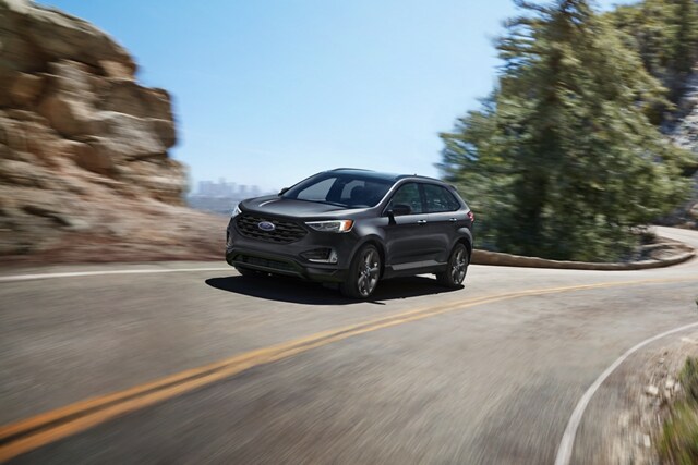 2024 Ford Edge® SEL in Carbonized Gray being driven on a curvy road with city in background