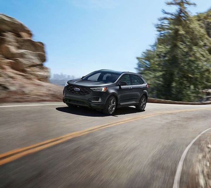2024 Ford Edge® in Carbonized Gray driving on a road overlooking a city