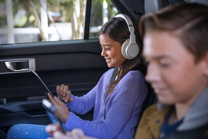 Two children use tablets in the back seat of a Ford vehicle using the vehicle’s Wi-Fi