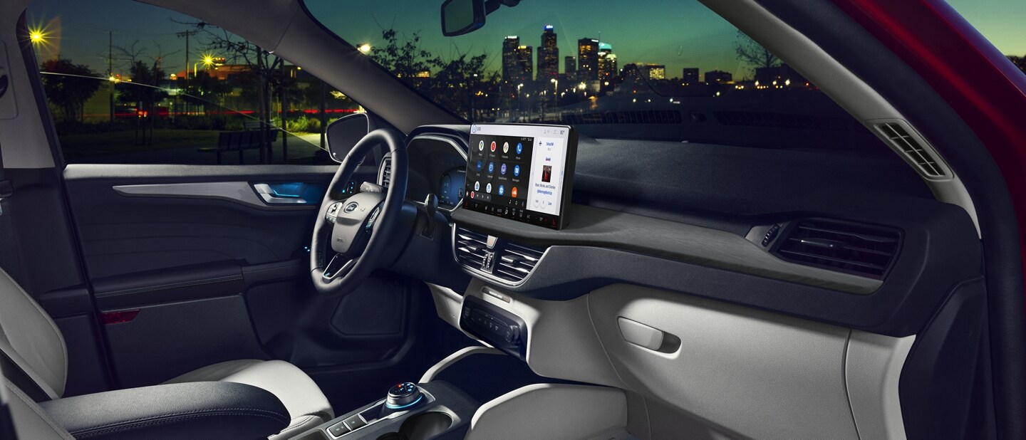 Una Ford Escape® 2023 en Rapid Red de noche, con la puerta del lado del pasajero abierta con el paisaje urbano de fondo