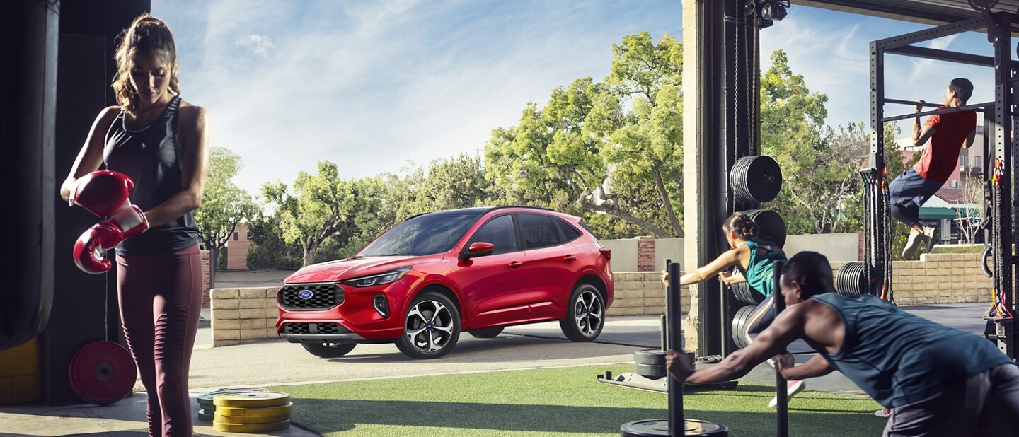 Una Ford Escape® 2023 en Rapid Red Metallic Tinted Clearcoat (pintura con costo adicional) estacionada frente a un concurrido centro de entrenamiento