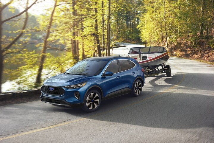 2023 Ford Escape® in Atlas Blue towing a boat along a river road