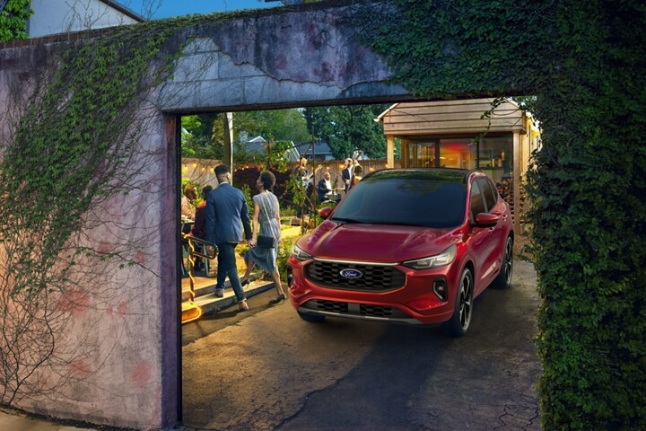 Una Ford Escape® Rapid 2023 en Red Metallic Tinted Clearcoat estacionada de noche en un camino de entrada con una fiesta de fondo