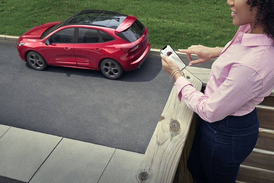 Person holds a smartphone on a porch overlooking a 2023 Ford Escape® in Rapid Red Metallic Tinted Clearcoat