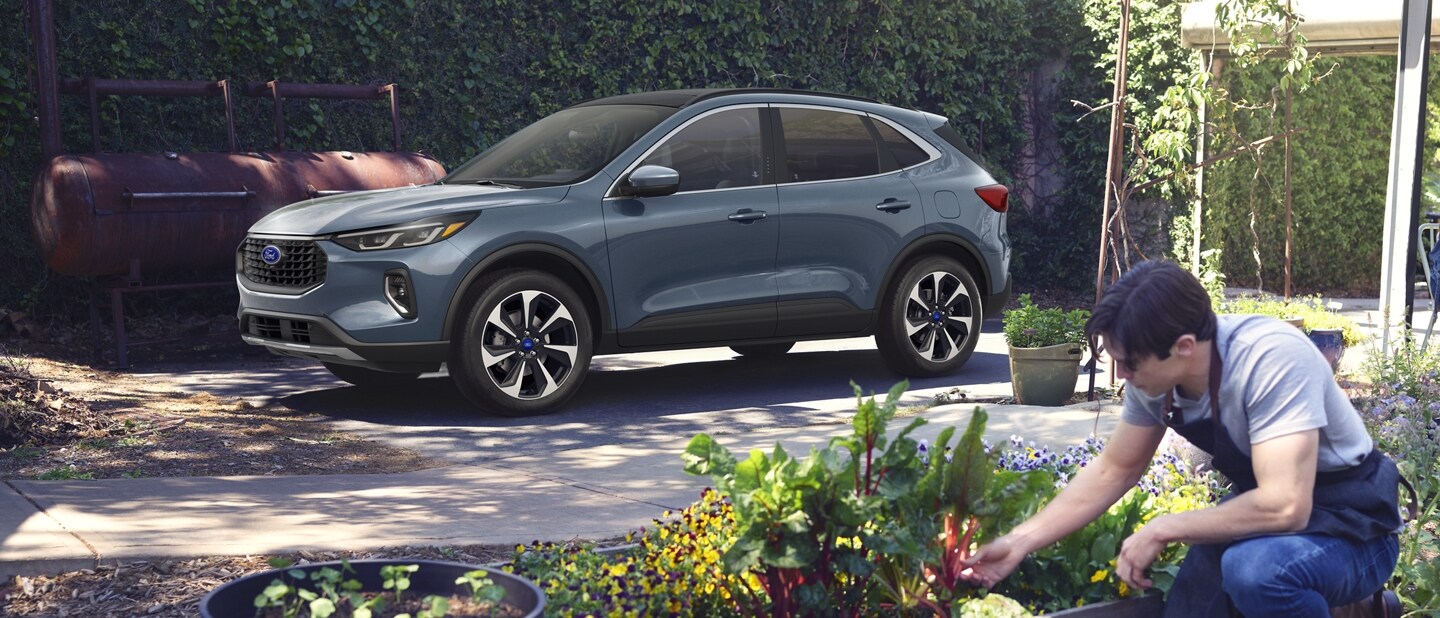 Una Ford Escape® 2023 en Vapor Blue Metallic estacionada en un jardín mientras un hombre trabaja con las plantas