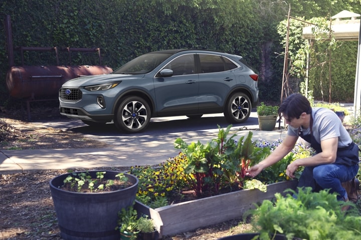 Una Ford Escape® 2023 en Vapor Blue Metallic estacionada en un jardín mientras un hombre trabaja con las plantas