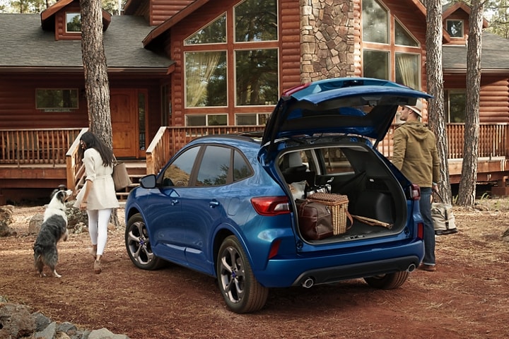 Una Ford Escape® 2023 en Atlas Blue estacionada frente a una cabaña mientras una mujer descarga equipaje