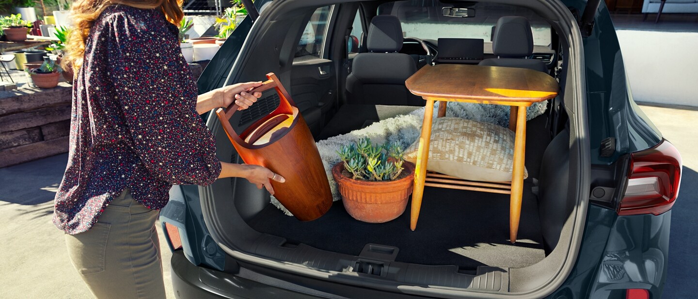 A woman loading the cargo area of a blue 2024 Ford Escape