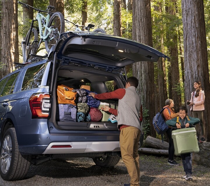 A family unloading gear from a 2023 Ford Expedition SUV parked in the woods