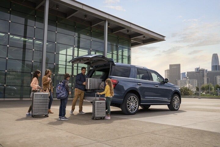A family unloads luggage from a 2023 Ford Expedition SUV parked in front of an urban building