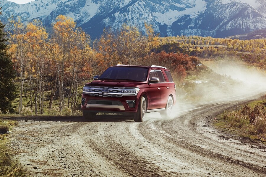 A 2023 Ford Expedition being driven on a dirt road with mountains behind it