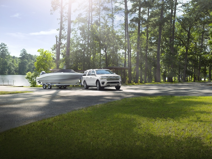 A 2024 Ford Expedition SUV towing a speed boat on a road near a wooded area