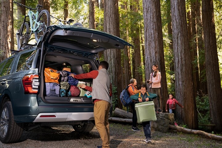A family unloading gear from a 2024 Ford Expedition SUV parked in the woods