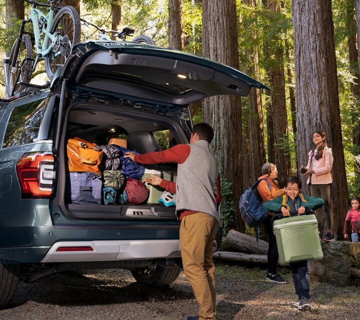 A 2024 Ford Expedition being loaded up with bags and items into its cargo space by a family in the woods
