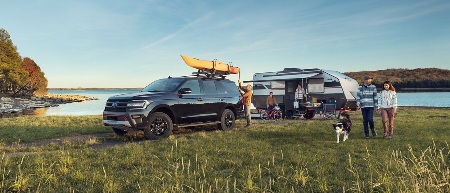 A 2024 Ford Expedition Timberline parked by a lake with a camper and family