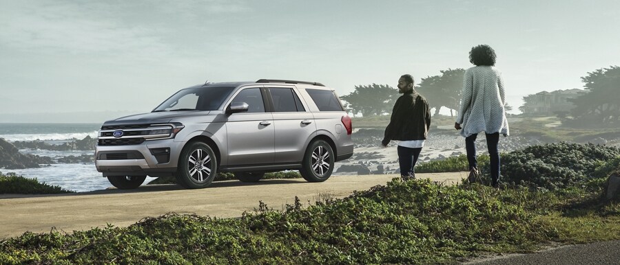 A 2024 Ford Expedition XLT parked next to ocean as a couple walks towards it