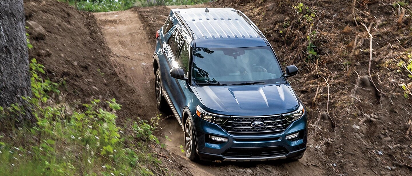 A 2021 Ford Explorer Limited in Blue being driven down a steep dirt hill in a woodsy environment