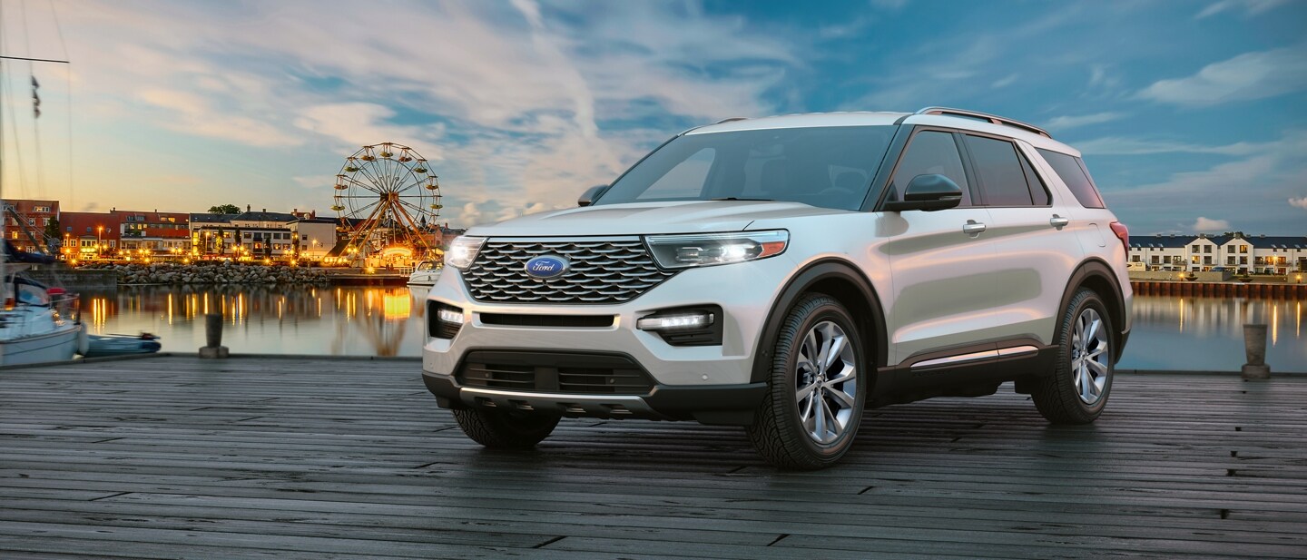 A 2023 Ford Explorer® Platinum with Adaptive LED headlamps on a pier with a fair in the background