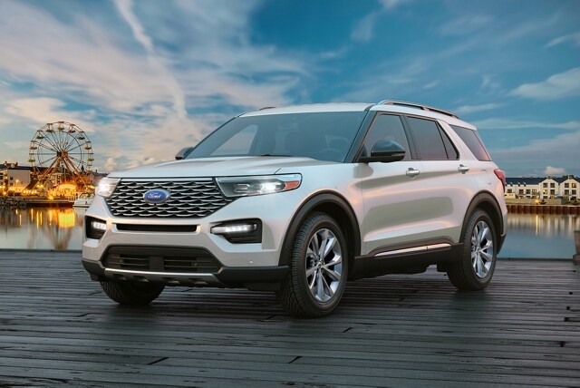 A 2023 Ford Explorer® Platinum with Adaptive LED headlamps on a pier with a fair in the background