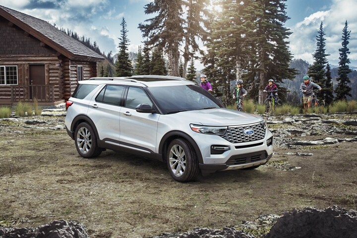 El modelo Ford Explorer® Platinum 2023 estacionado junto a una cabaña mientras se acerca una familia con bicicletas para montaña