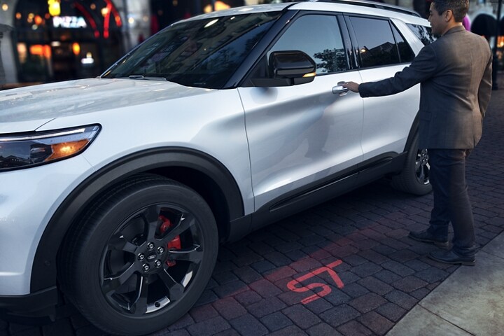 El modelo Ford Explorer® ST 2023 con faros con proyección ST iluminando el suelo debajo de una persona que está por tomar la manija