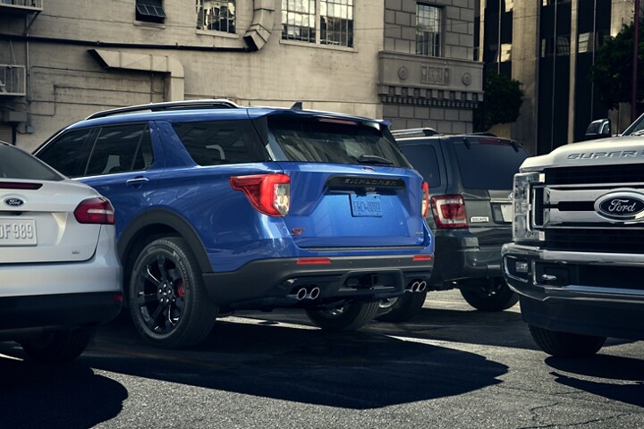 Una SUV Ford Explorer® ST 2023 en un lugar de estacionamiento mientras por atrás pasa una camioneta Ford Super Duty®