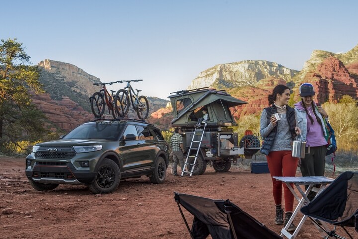 Una SUV Ford Explorer® Timberline® 2023 en Forged Green Metallic estacionada en el desierto con una carpa en la parte superior de un remolque y una familia