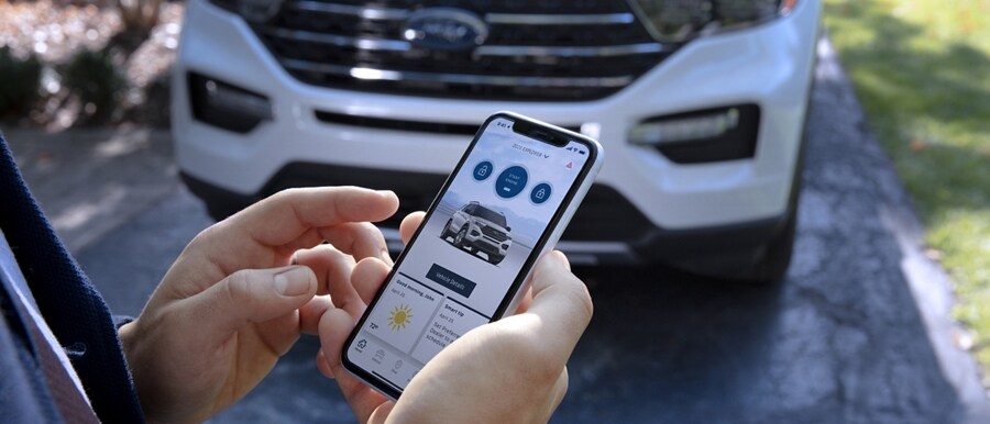 Una persona de pie delante de una SUV Ford Explorer® 2023 sosteniendo un smartphone que muestra la Aplicación FordPass®
