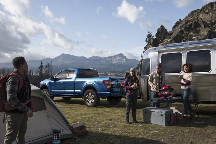 A group of friends grilling at a campsite near a 2021 Ford f 1 50 and camper
