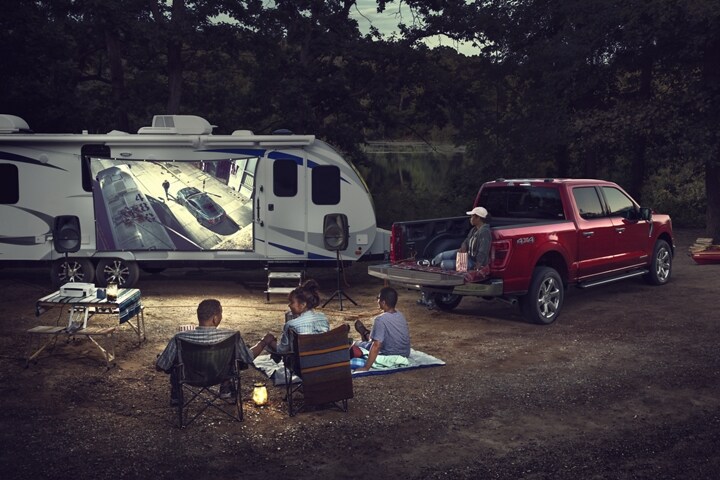 A family watching a movie being projected onto a screen outside a trailer near a 2021 Ford F 1 50