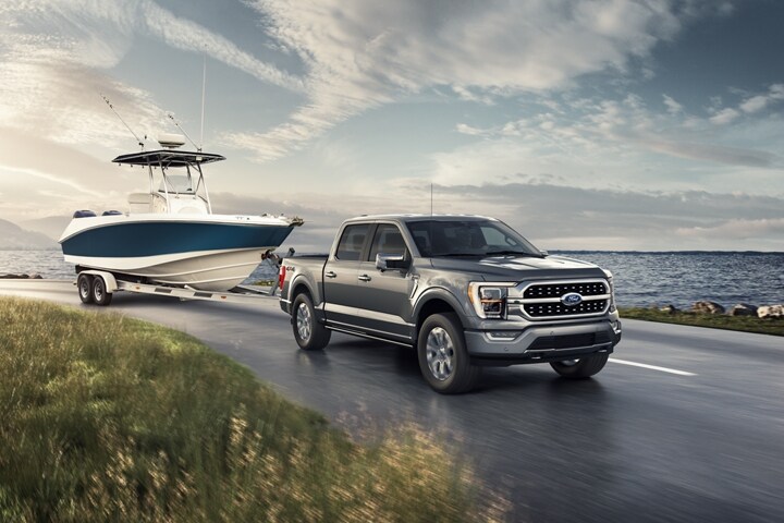 A 2021 Ford F 1 50 Platinum parked by a large body of water with a boat in tow