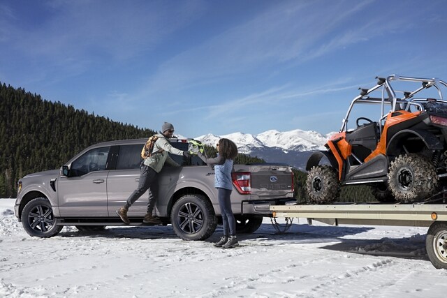 Two people using the extended running boards to load up a 2021 Ford® F-150 in the snow
