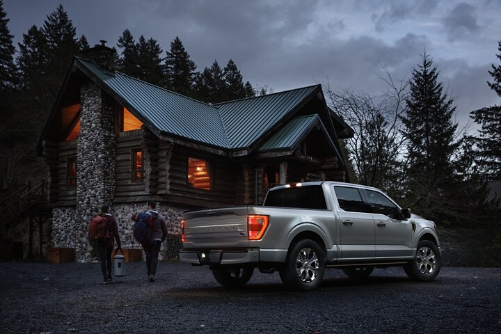 Two people approaching a remote cabin with a 2023 Ford F-150® Platinum parked nearby