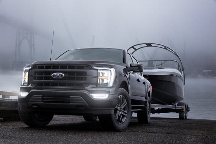 A 2023 Ford F-150® parked with its LED headlamps on at a boat ramp at dusk