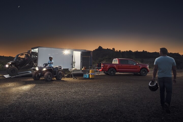A 2023 Ford F-150® LARIAT parked with a trailer towing sand dune bikes with two people