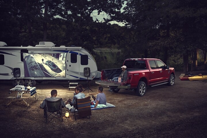 A family watching a movie being projected onto a screen outside a trailer near a 2023 Ford F-150®