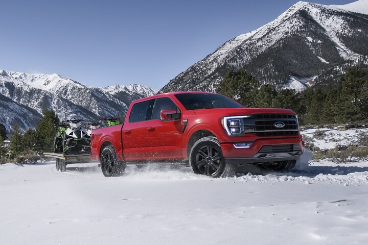 A 2023 Ford F-150® towing snowmobiles on a trailer through the snow