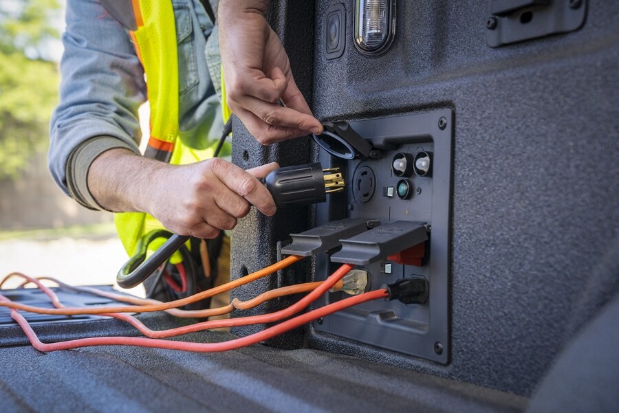 Un hombre enchufando un cable en el tomacorriente de 120 voltios en la plataforma de una Ford F-150® 2023
