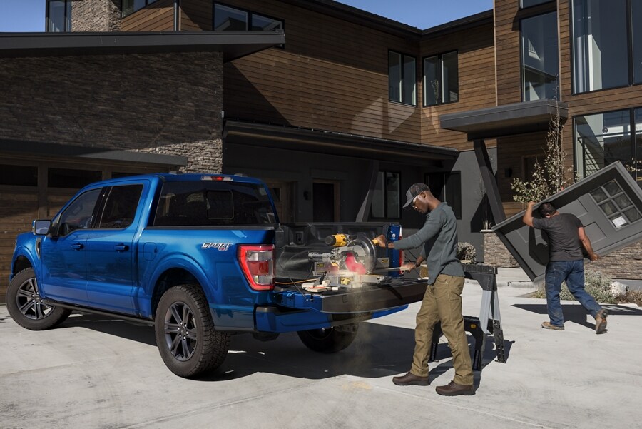 Un hombre cortando madera con una sierra eléctrica sobre la puerta trasera de una Ford F-150® XLT SuperCrew® 2023