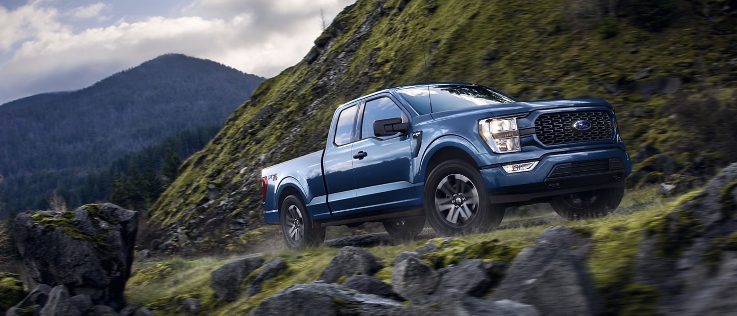 Una Ford F-150® XLT 2023 en Atlas Blue andando por un camino de montaña