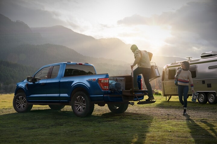 A couple loading camping gear into the bed of their 2023 Ford F-150® near their campsite