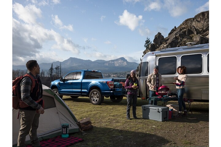 A group of friends grilling at a campsite near a 2023 Ford F-150® and camper