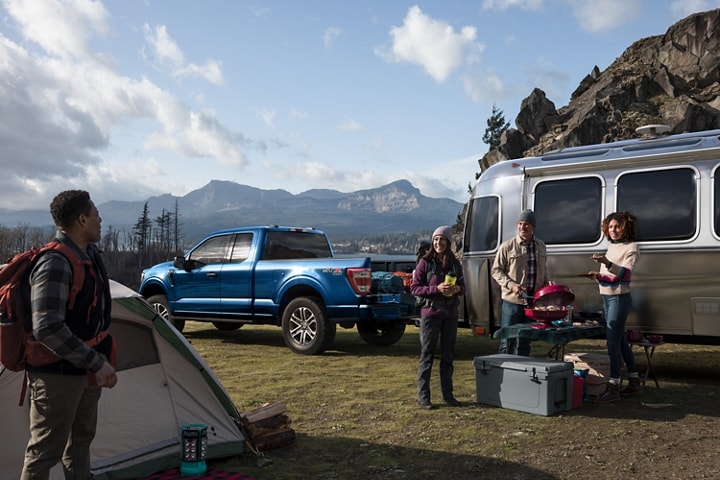 A group of friends grilling at a campsite near a 2023 Ford F-150® and camper