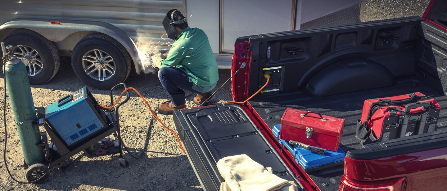 Person welding a trailer near a 2023 Ford F-150® while using the Pro Power Onboard™ feature