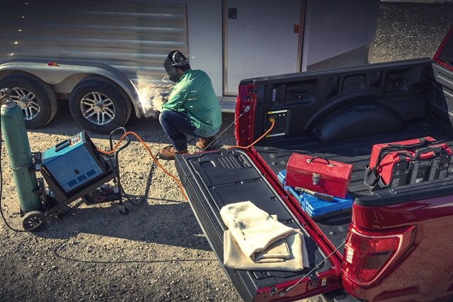 Person welding a trailer near a 2023 Ford F-150® while using the Pro Power Onboard feature