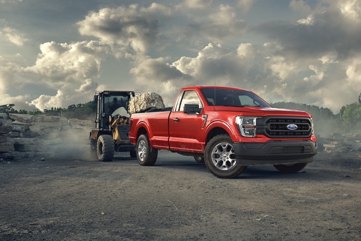 A multi-terrain loader loading a large rock into the bed of a 2023 Ford F-150®