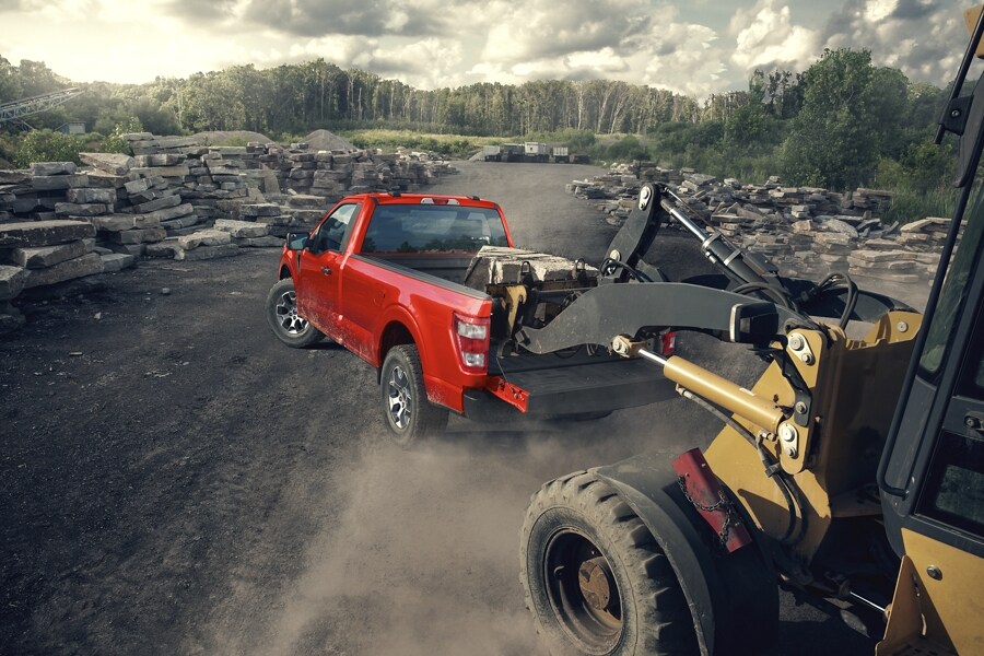 Image of a tractor loading construction materials into the rear tailgate area of a 2023 Ford F-150® at a work site