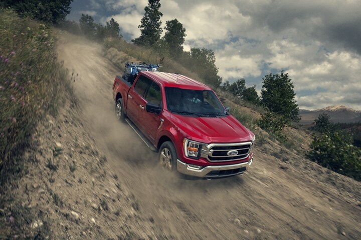 A 2023 Ford F-150® with an ATV in the bed being driven down a dirt hill